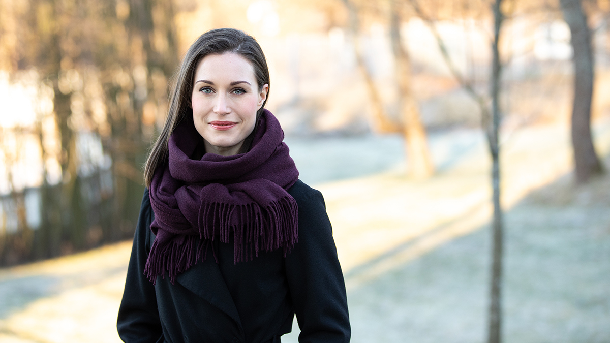 Prime Minister Sanna Marin standing outside wearing a black coat and a purple scarf.