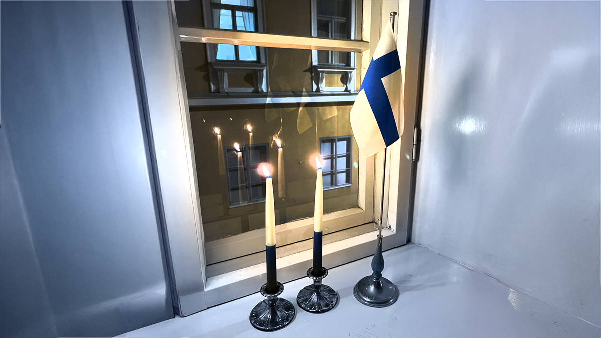 Ikkunalla kaksi kynttilää ja Suomen lippu.