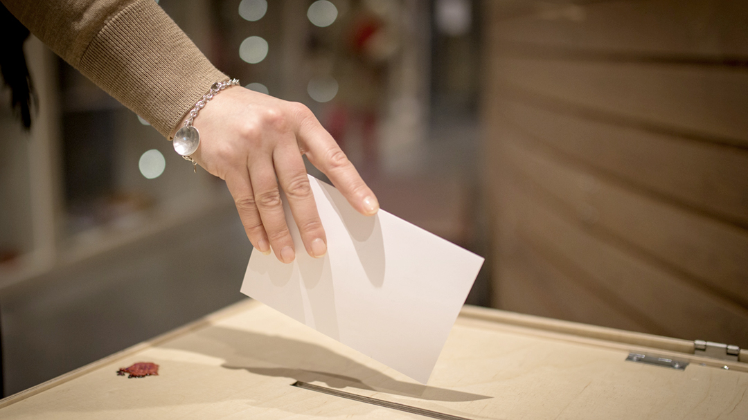 A person is placing a ballot paper in the ballot box.
